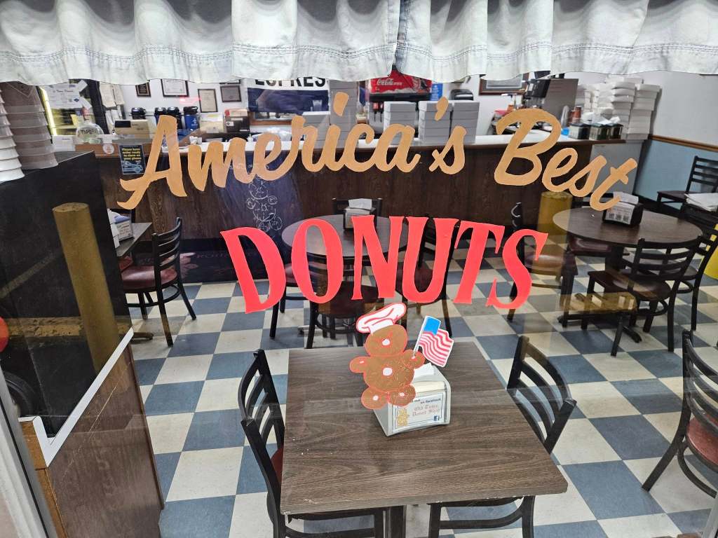 Interior view of Old Town Donuts in Florissant, Missouri, with window signage reading "America's Best Donuts" and a patriotic donut character on a table.
