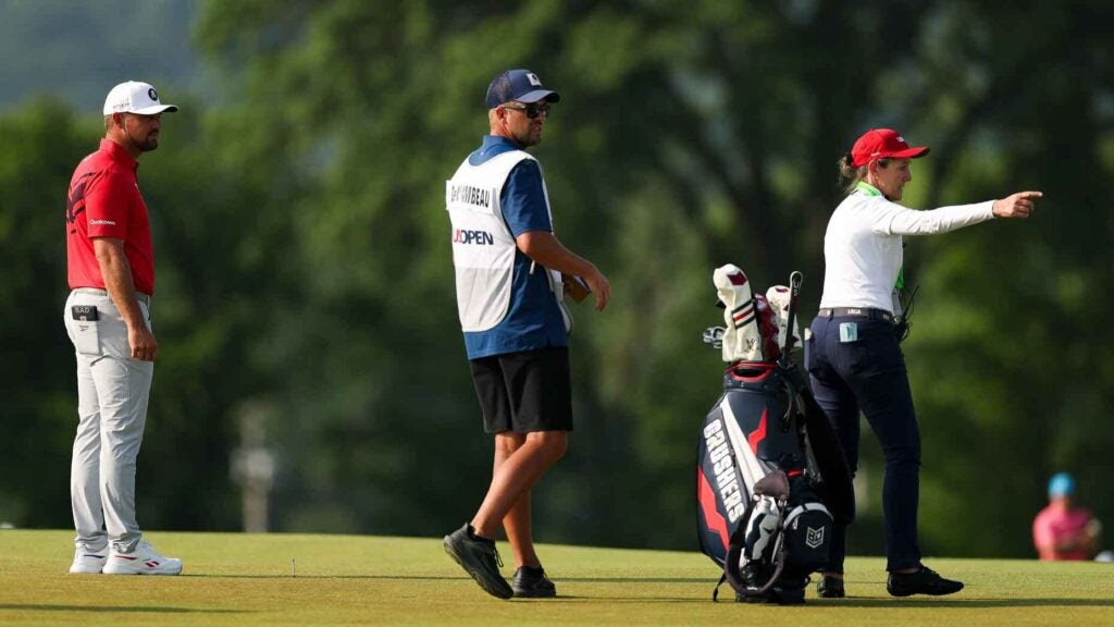 Bryson DeChambeau, his caddie, and a USGA rules official discuss relief options during the first round of the 2025 U.S. Open at Oakmont Country Club.