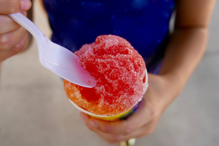 Close-up of a person holding a red and orange shaved ice with a white spoon