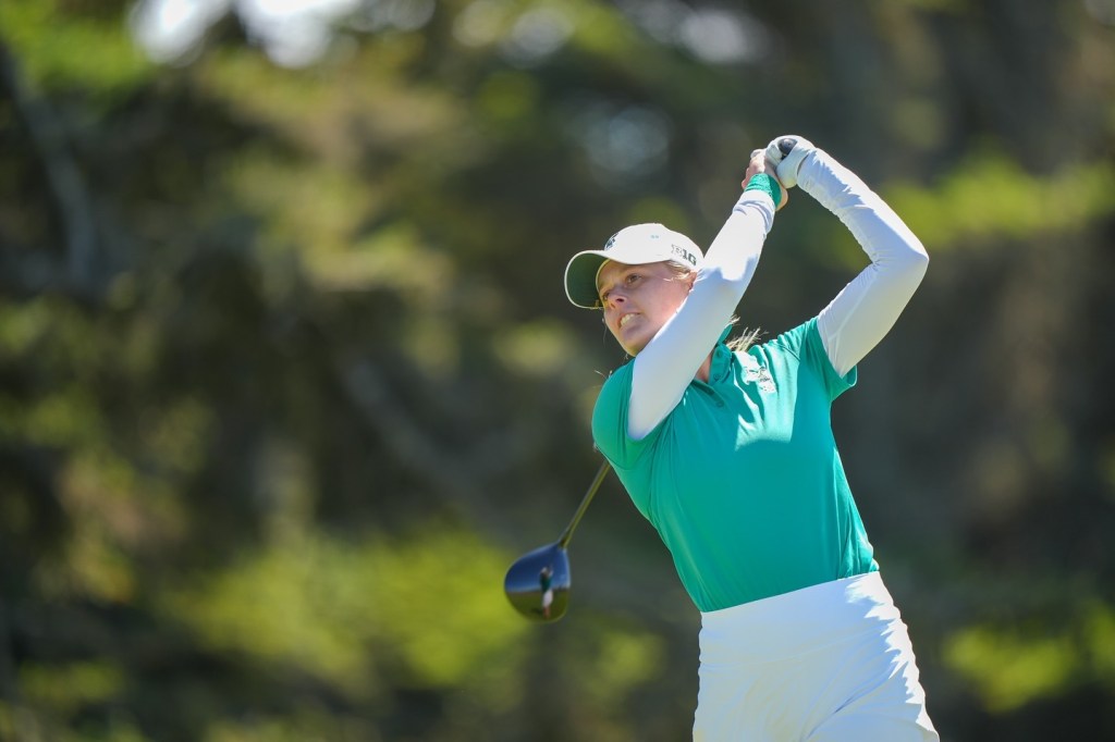 Brooke Biermann follows through on her golf swing during the U.S. Women’s Amateur Championship, wearing a green shirt and white skirt.