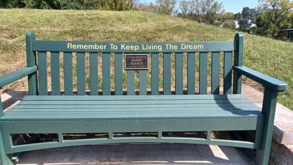 Green memorial bench with the inscription “Remember To Keep Living The Dream” in honor of Randy Brandt